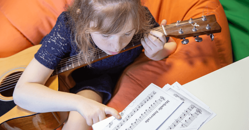 Young girl reading sheet music while playing guitar